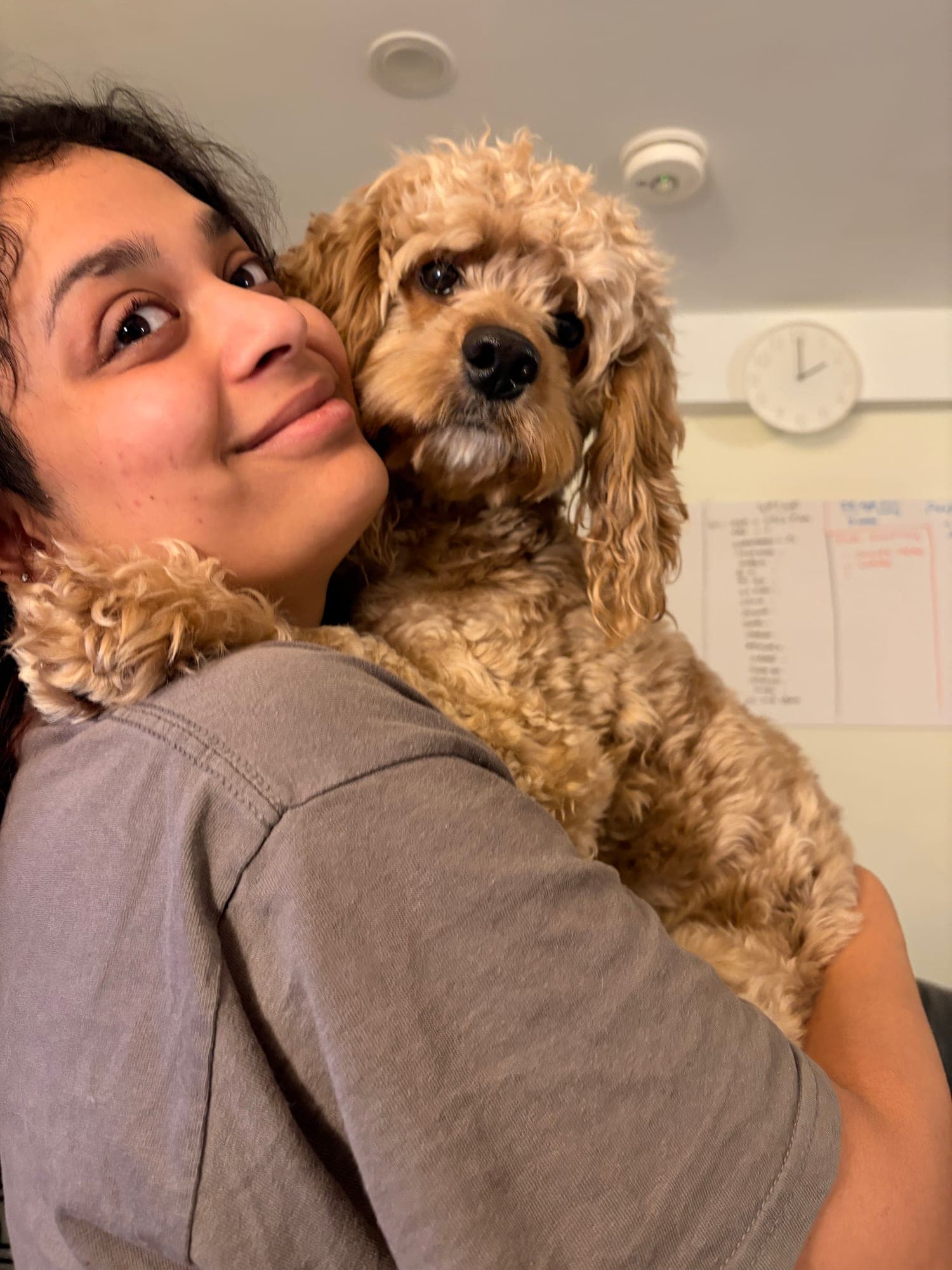 Khushi holding a curly apricot dog over her shoulder, their cheeks pressed together, both looking at the camera.