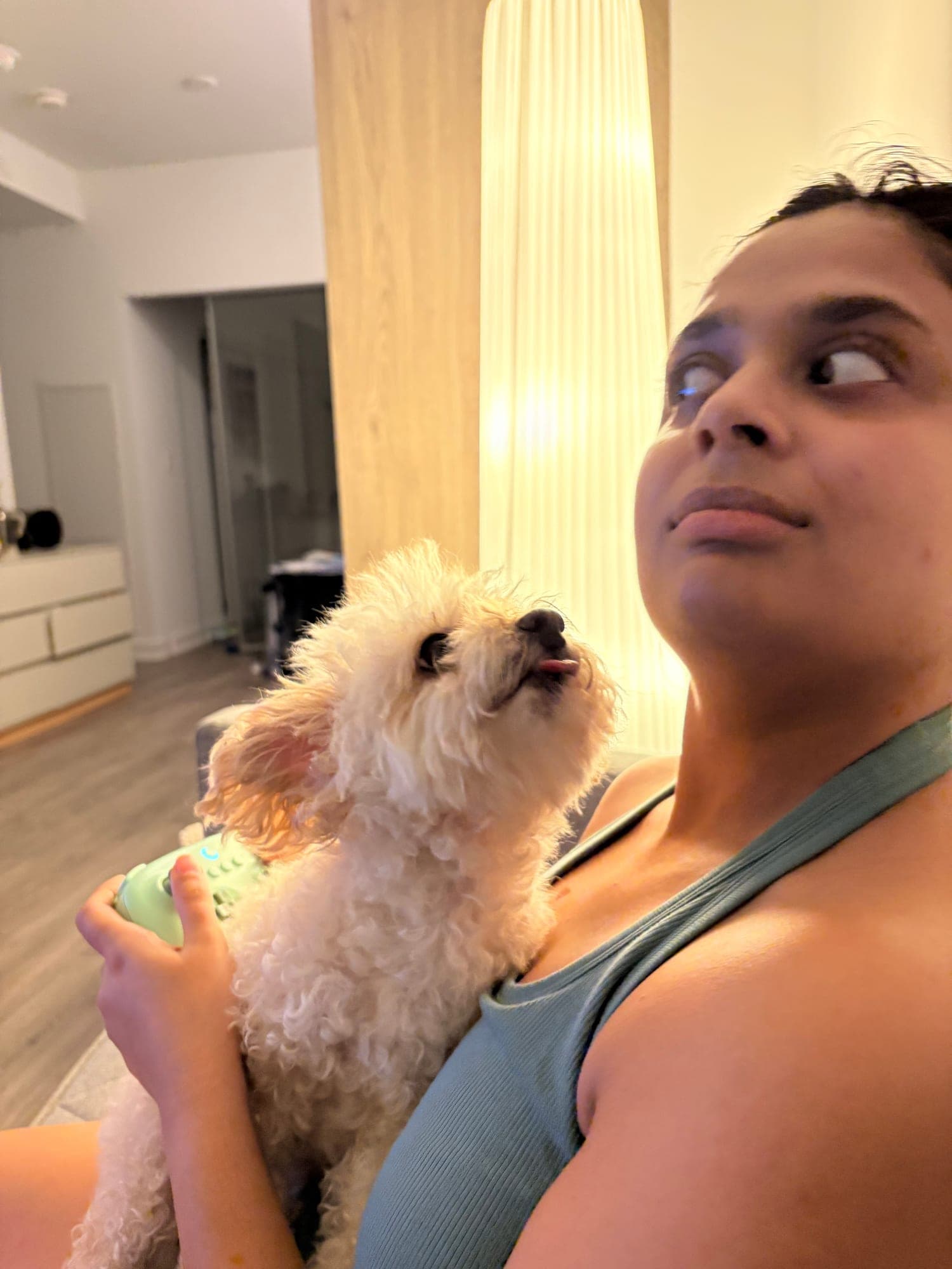 Khushi giving a sideways, sceptical look while a small fluffy cream dog sits against her chest looking up.
